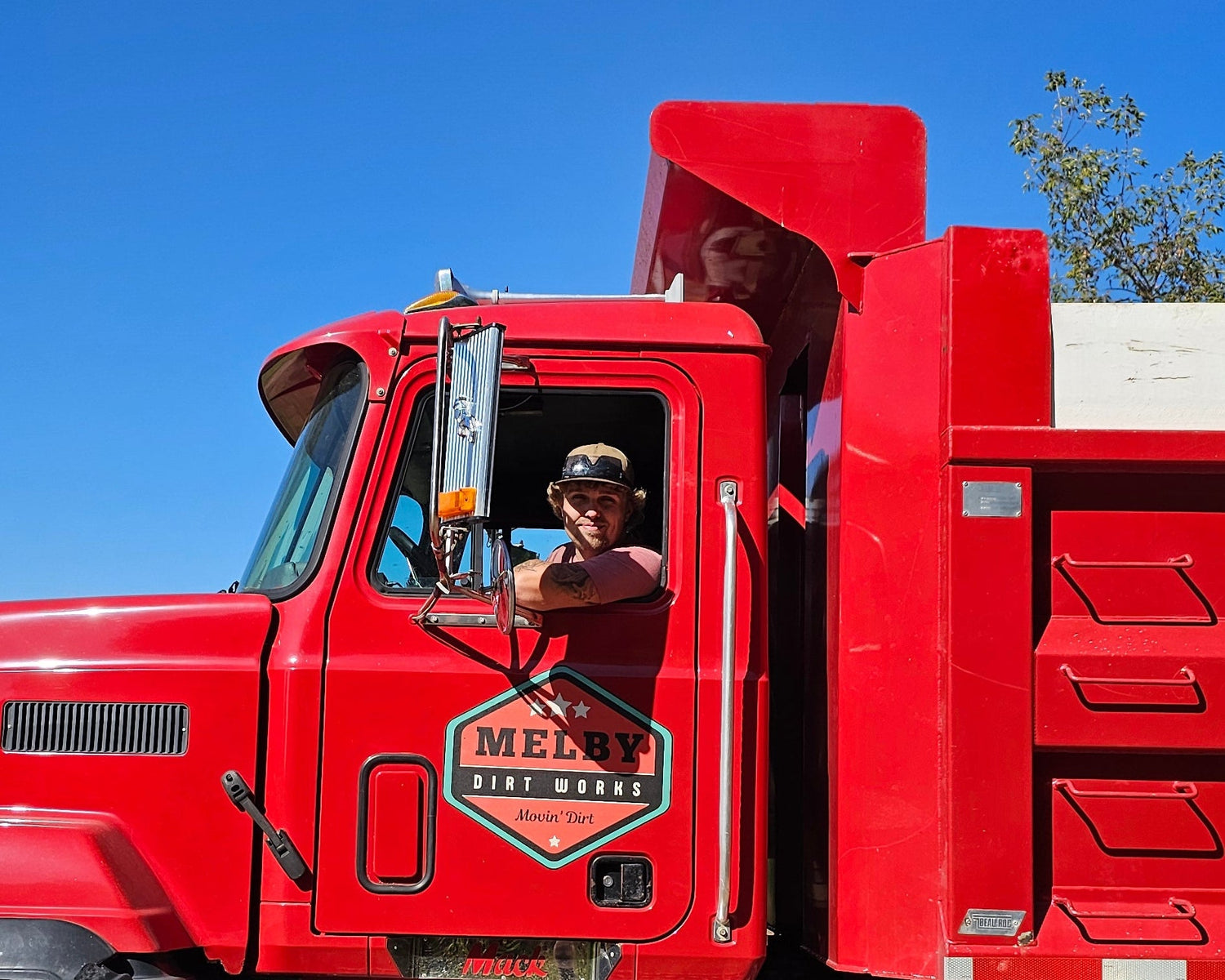 Red dump truck on a dirt road with trees in the background